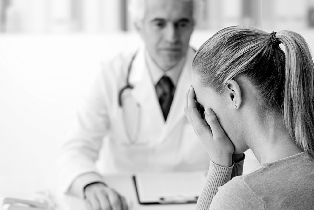 Doctor frowning at a woman in front of him with her hands over her face.
