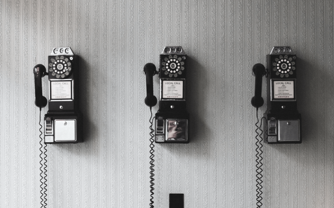 3 black, vintage pay phones on the wall.