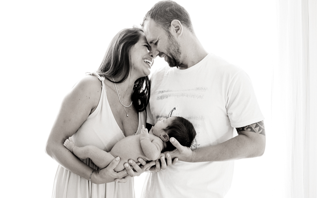 A husband and wife smile at one another as they hold their newborn baby.