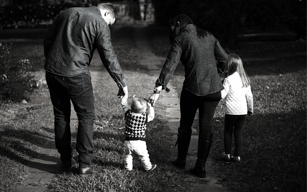 A husband and wife hold their children's hands as they walk together.