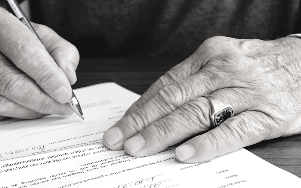 A man with a ring on his finger signs a medical form. 