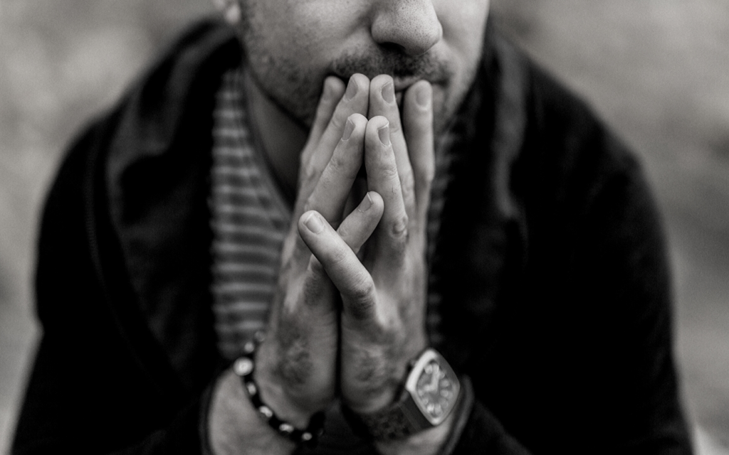 A man sits with his hands folded near his face.