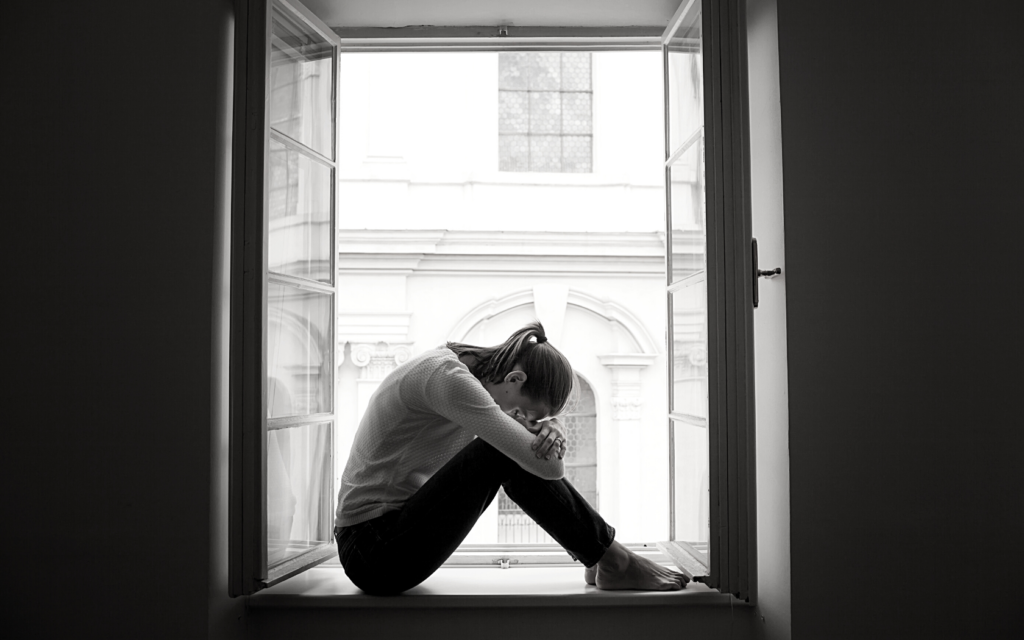A woman sits with her head cradling her knees looking depressed. 