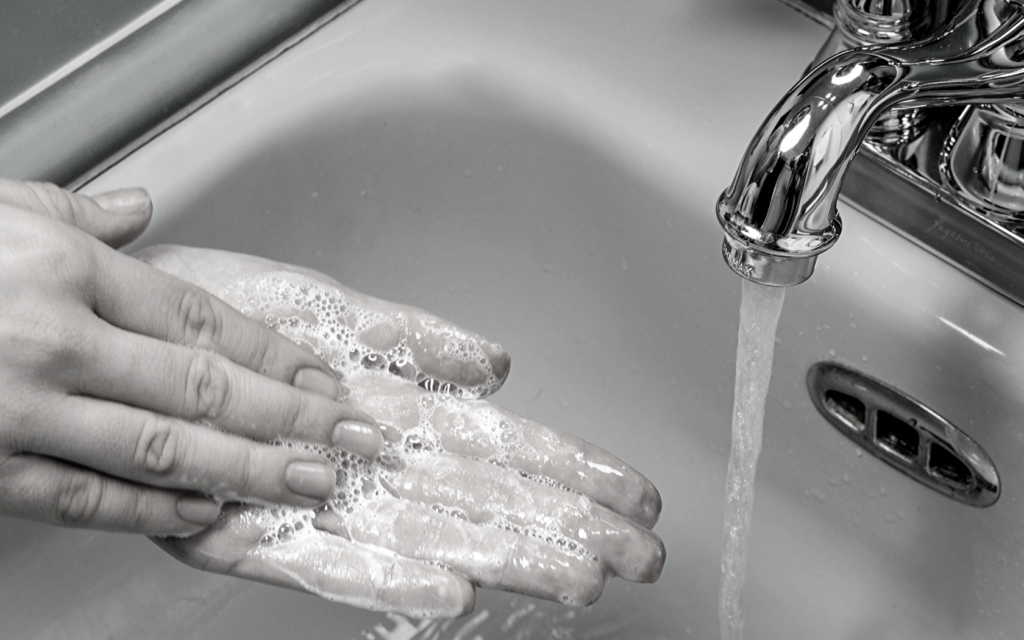 A woman lathers soap in her hands underneath a faucet.