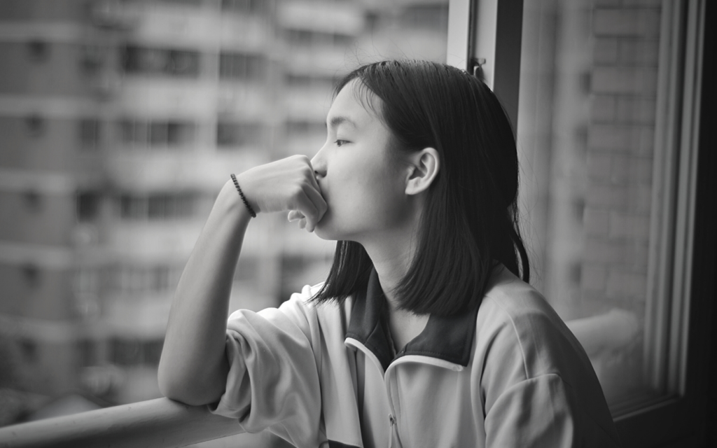 A young woman stares out a window in contemplation.