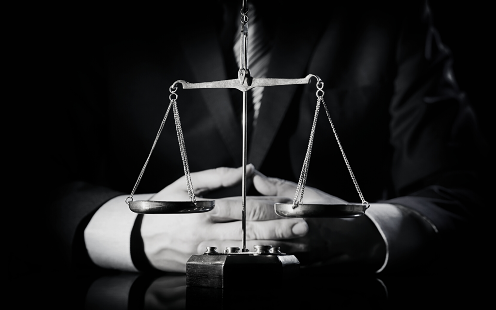 Image of the scales of justice and a person with a suit and tie in the background. 