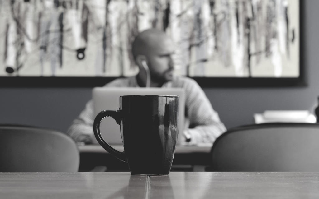 A man sits at a coffee shop working with a coffee mug in front of him.