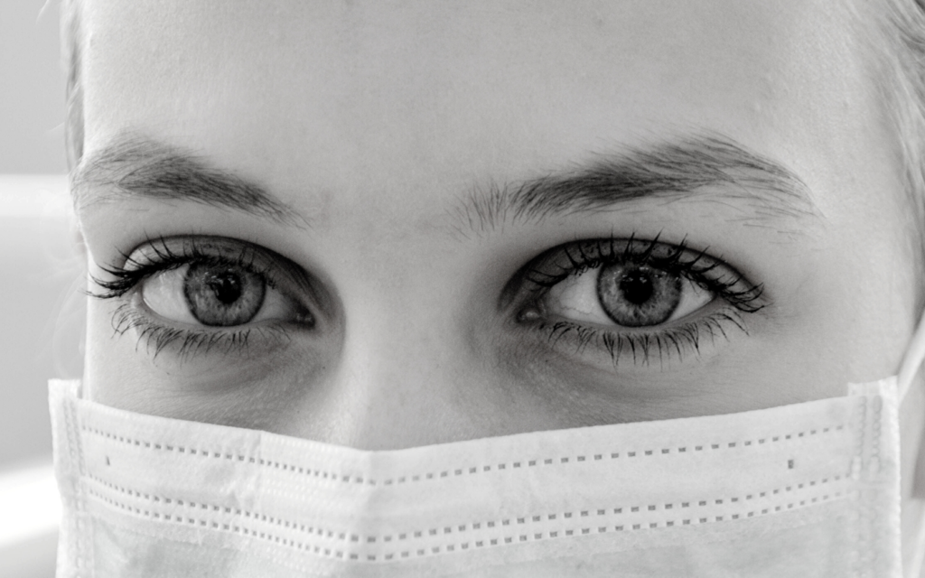 A woman wearing a surgical mask looks directly at the camera. 
