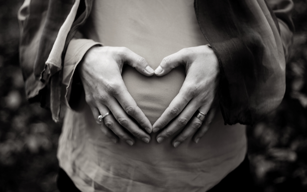 A pregnant woman holds her baby bump in the shape of a heart. 
