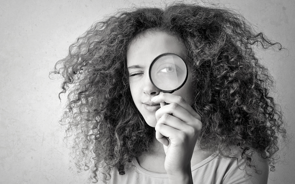 Woman holds magnifying glass up to her face.