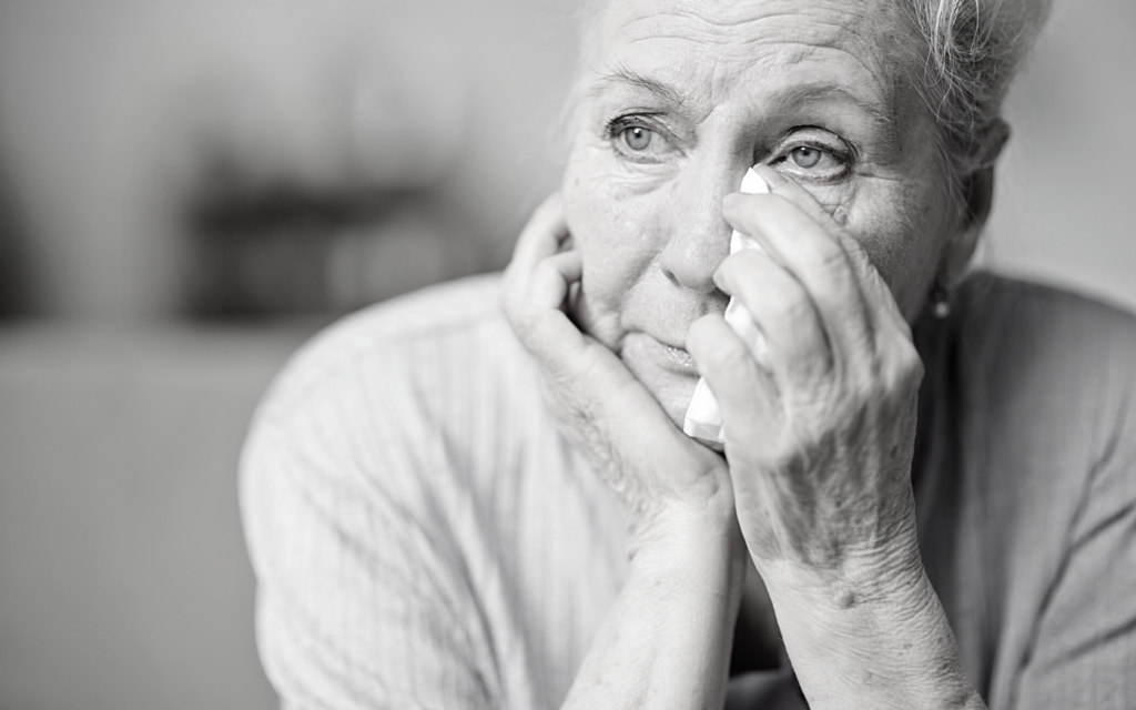 Older woman wipes tears away.