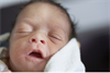 Newborn baby yawning, wrapped in a white blanket.