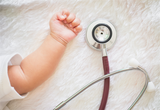 Baby's hand closed with stethoscope next to her.