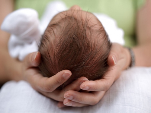 A mother holding newborn baby's head in her hands.