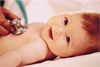 Cute baby smiling as the doctor checks her heart with a stethoscope.