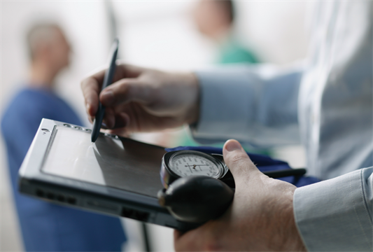 Doctor writing on tablet, with nurses talking in the background.