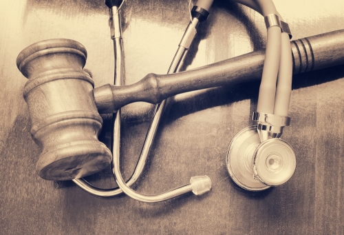 Gavel and stethoscope intertwined, laying on a courtroom table.