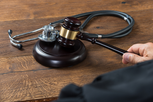 Gavel resting on courtroom desk in judge's hand, with stethoscope next to it.