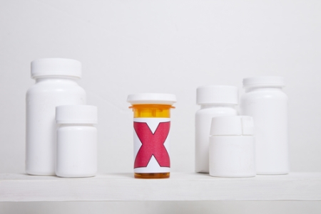 Blank white pill bottles flanking a pill bottle with a large red X printed on it