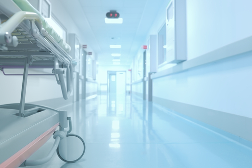 Hospital bed in the hallway of the hospital, two-way door in the distance.