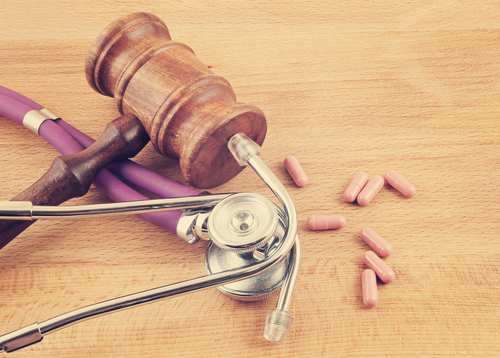 Gavel and stethoscope next to pink pills on wooden table.