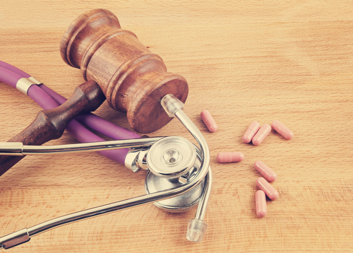 Gavel, stethoscope, and scattered pills lying on a desk