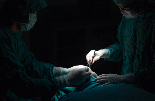 Two surgeons with scalpel and a medical tool working on unconscious patient. 