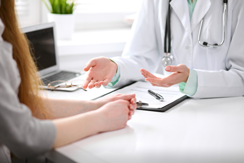 Doctor sitting at table with client, gesturing with hands.