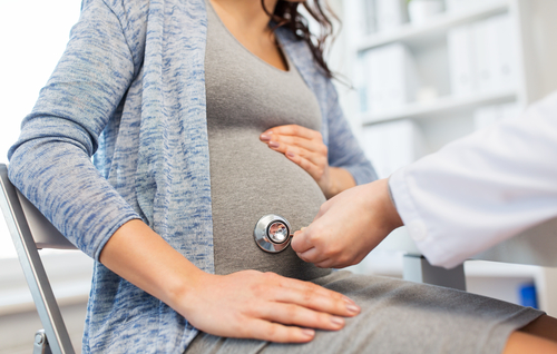 Pregnant woman getting baby's heart checked by a doctor with a stethoscope.