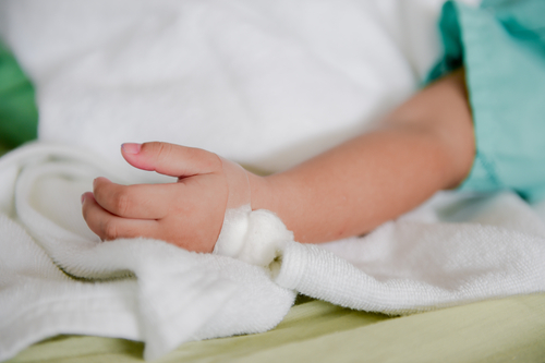 Baby's hand wrapped with a bandage & medical tape, resting on a white blanket.