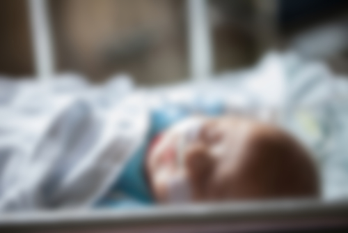 Newborn baby lying on hospital bed, photo blurred.