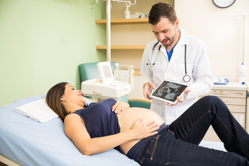Doctor showing a pregnant woman an ultrasound on an iPad while she lies on a patient table with her shirt pulled up