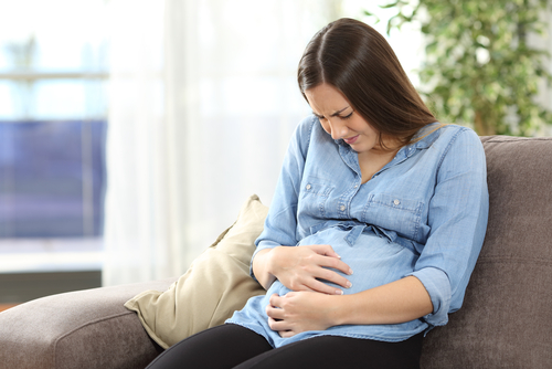 Pregnant mother sitting on couch and holding stomach in pain.