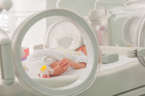 Newborn baby laying on hospital bed next to medical equipment.