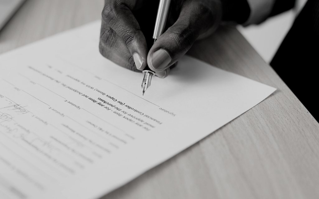 Man's hand signing agreement with pen.