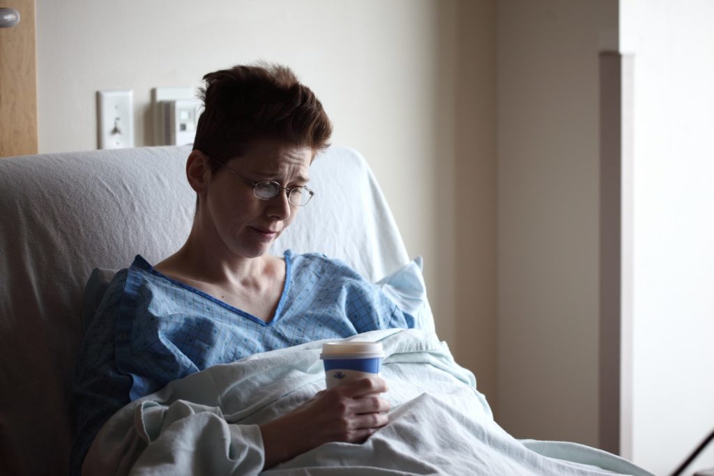 Sad woman laying in hospital bed with a coffee cup in her hand.