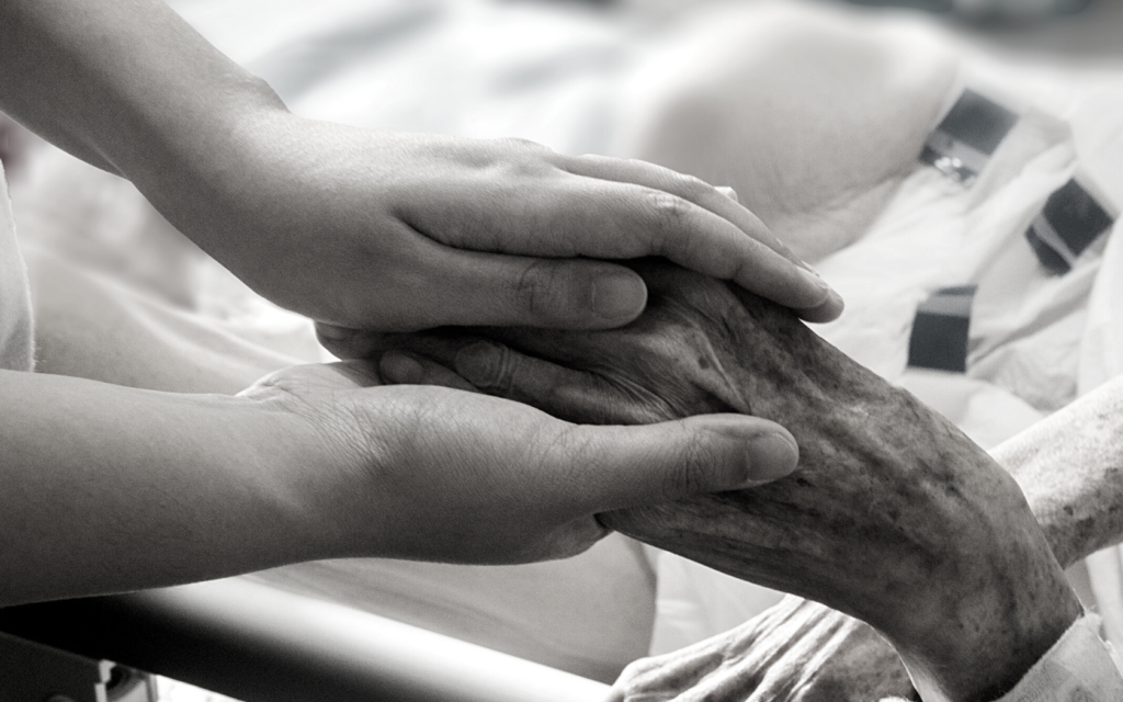 Caregiver holds elderly patient's hand.