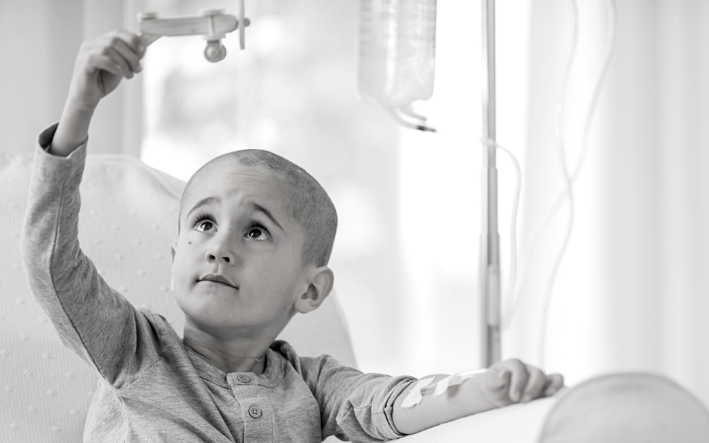 Little boy with leukemia plays in hospital bed.
