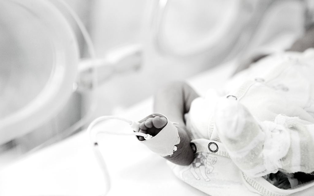 An infant with medical issues laying in a hospital bed.