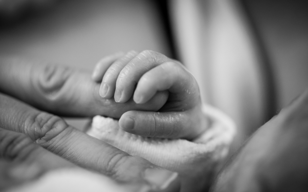 Newborn baby grips mother's finger.