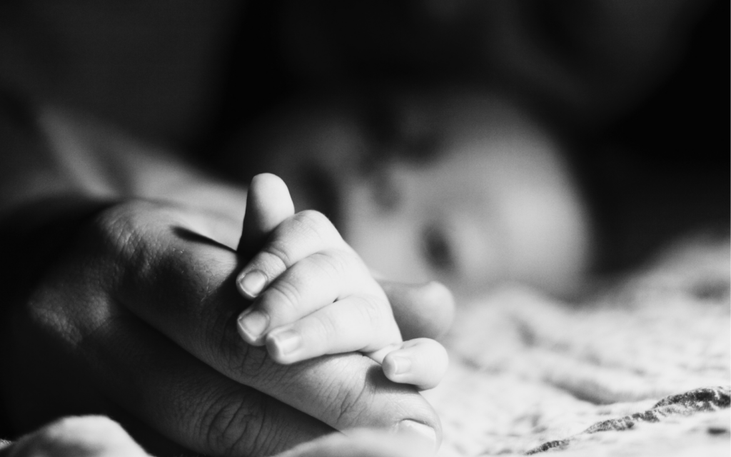 A baby holds its mother's hand.