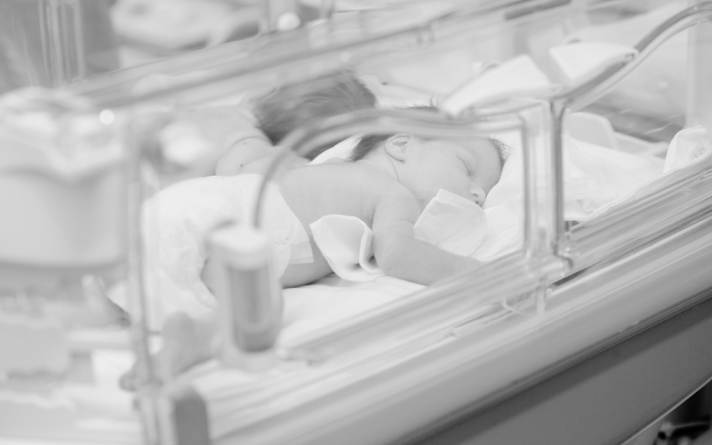 Newborn baby in NICU hospital bed.