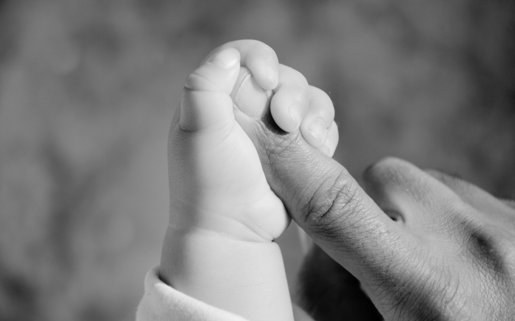 Toddler holds tight to parent's finger.