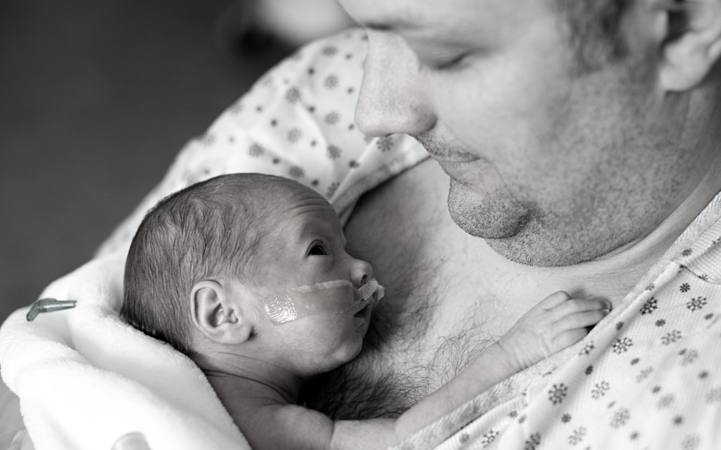 Father holds his newborn baby close to his chest.