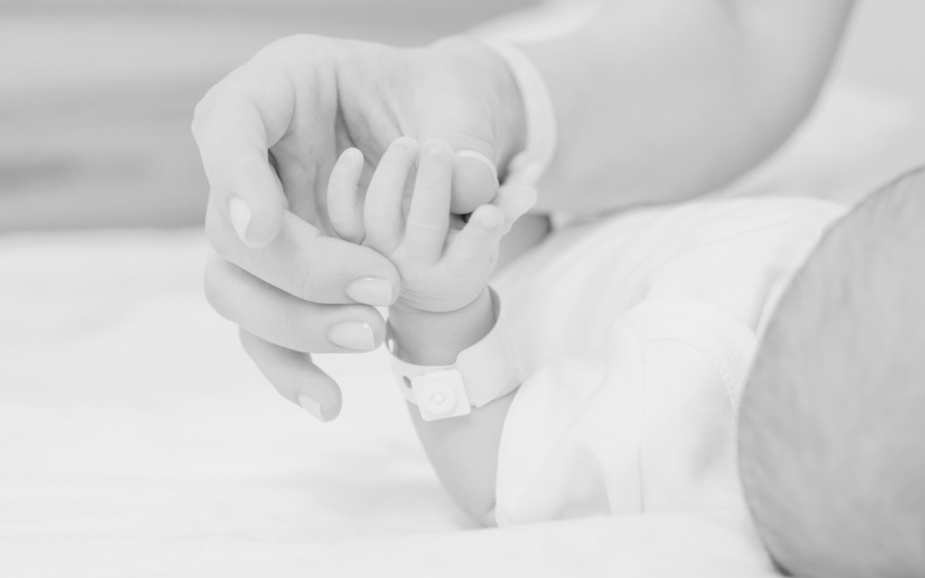 Mother holds newborn's hand.