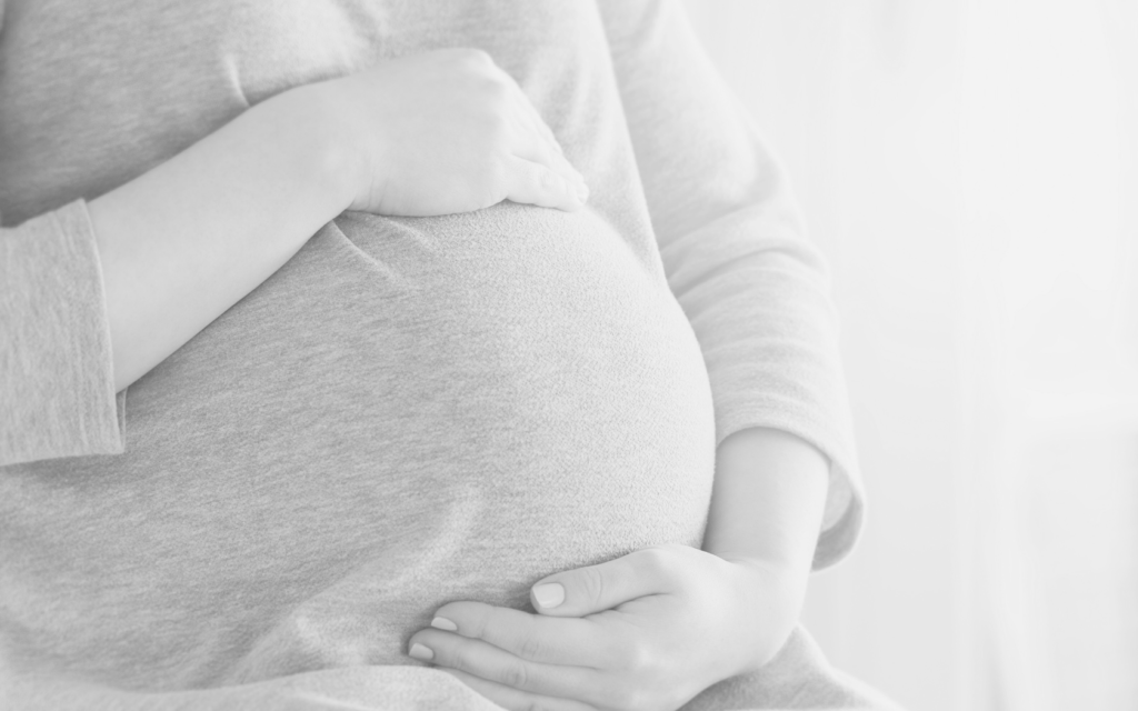 Woman cradles her pregnant belly.