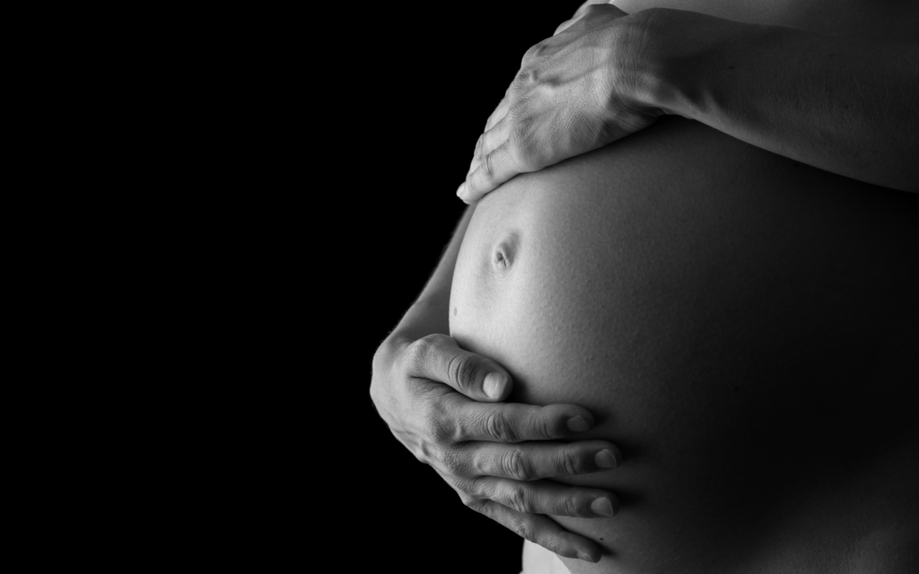 A woman gently cradling her pregnant belly with both hands.