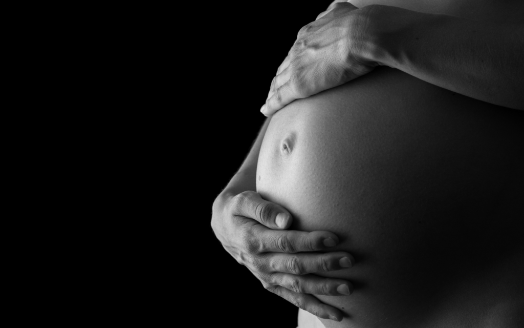 A woman gently cradling her pregnant belly with both hands.