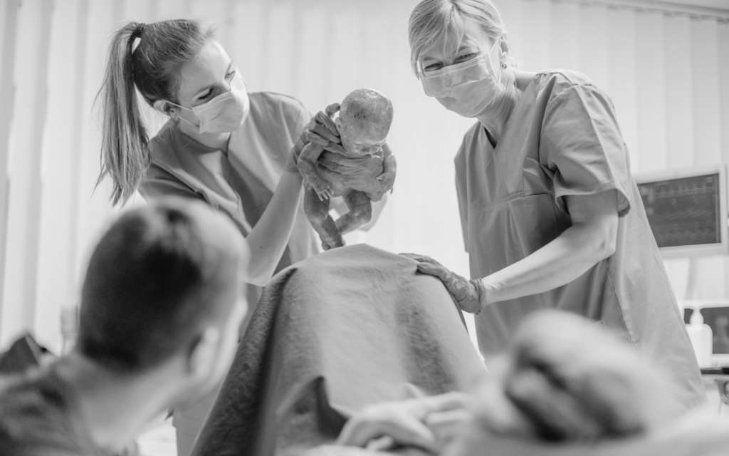 A doctor gently holds up the newborn baby for the mother to see immediately after delivery.