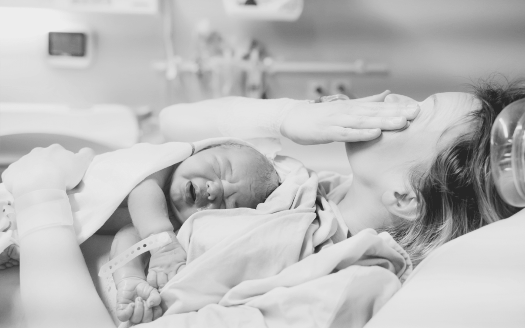 A mother holding her newborn baby after delivery, with tears of worry streaming down her face.